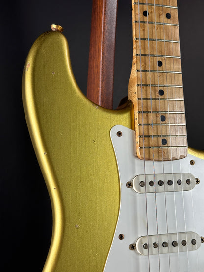 Close-up of a guitar with a gold body and wooden neck on a black background