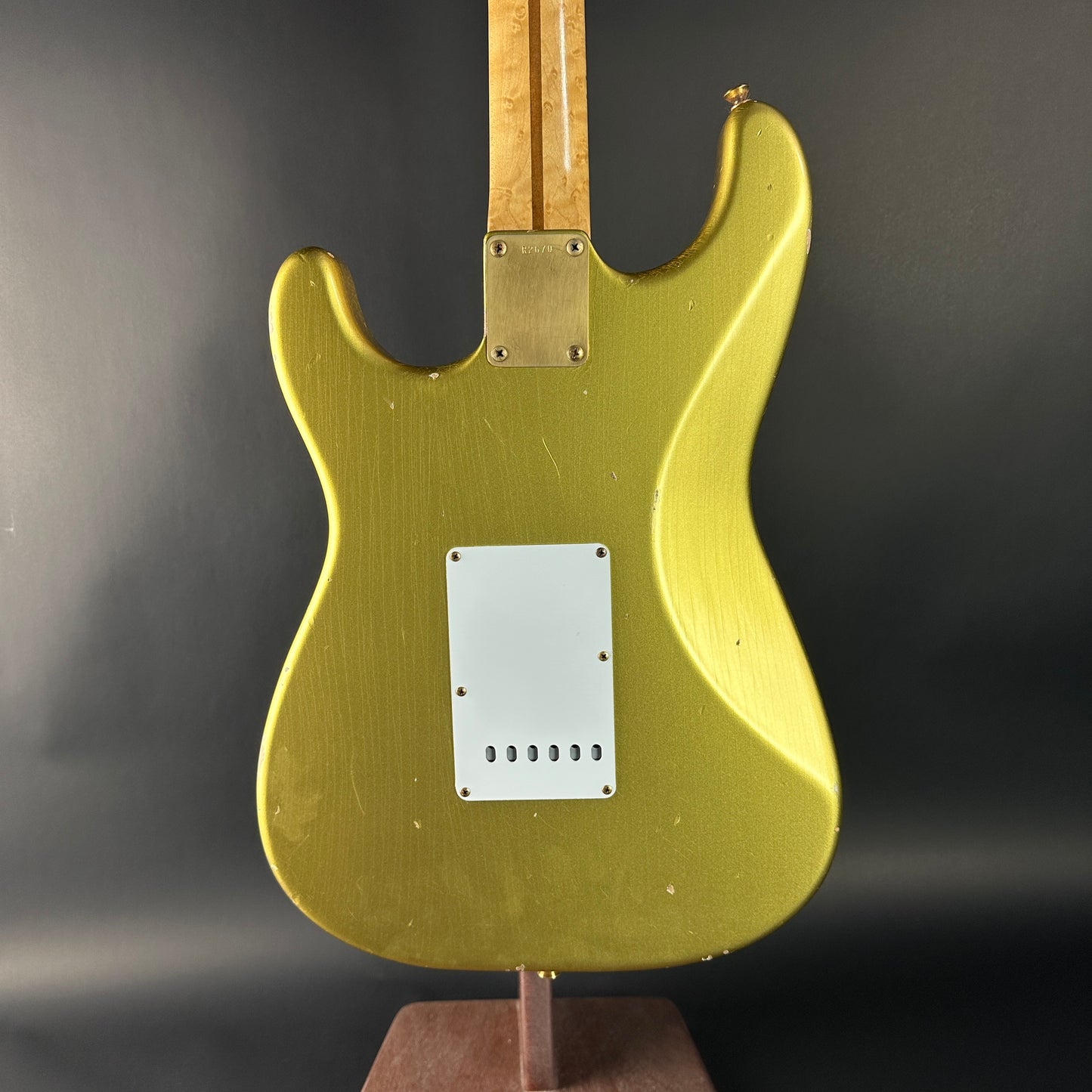 Gold electric guitar body on a stand against a dark background