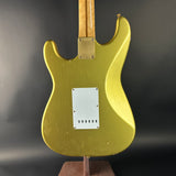 Gold electric guitar body on a stand against a dark background