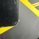 Close-up of a black rectangular object corner with a small screw fastener, showing scuffs and scratches on a dark gray surface with bold yellow diagonal stripes.