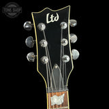 Close-up of the headstock of a black electric guitar with six silver tuning pegs and a white 'Ltd' logo, shown against a black background with a Tone Shop watermark in the upper left.