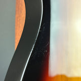 Extreme close-up of a glossy dark brown or black guitar body edge with visible scratches and dust on the finish, alongside warm wood grain and a bright reflective area.