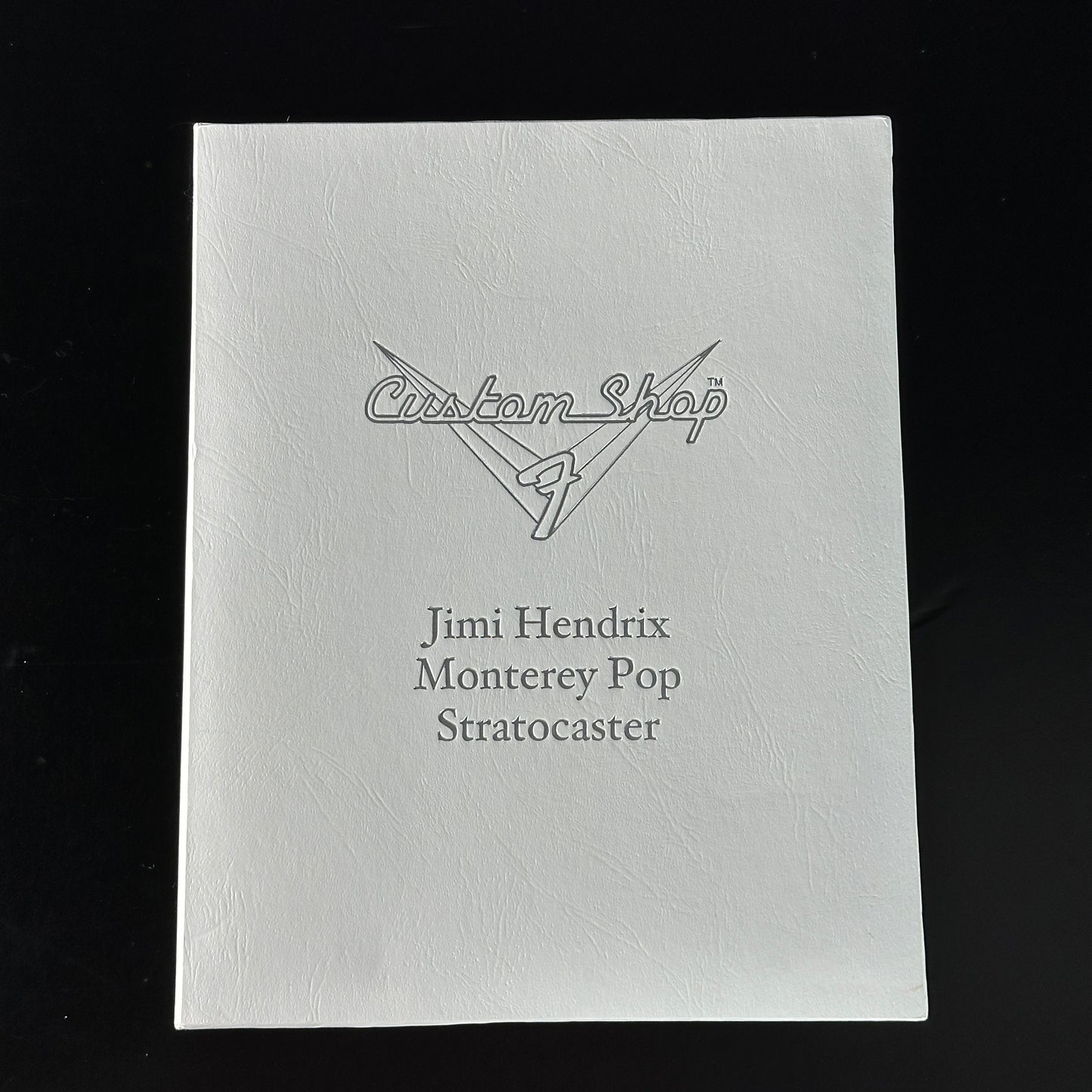 White guitar case with 'Custom Shop' and 'Jimi Hendrix Monterey Pop Stratocaster' text on a black background