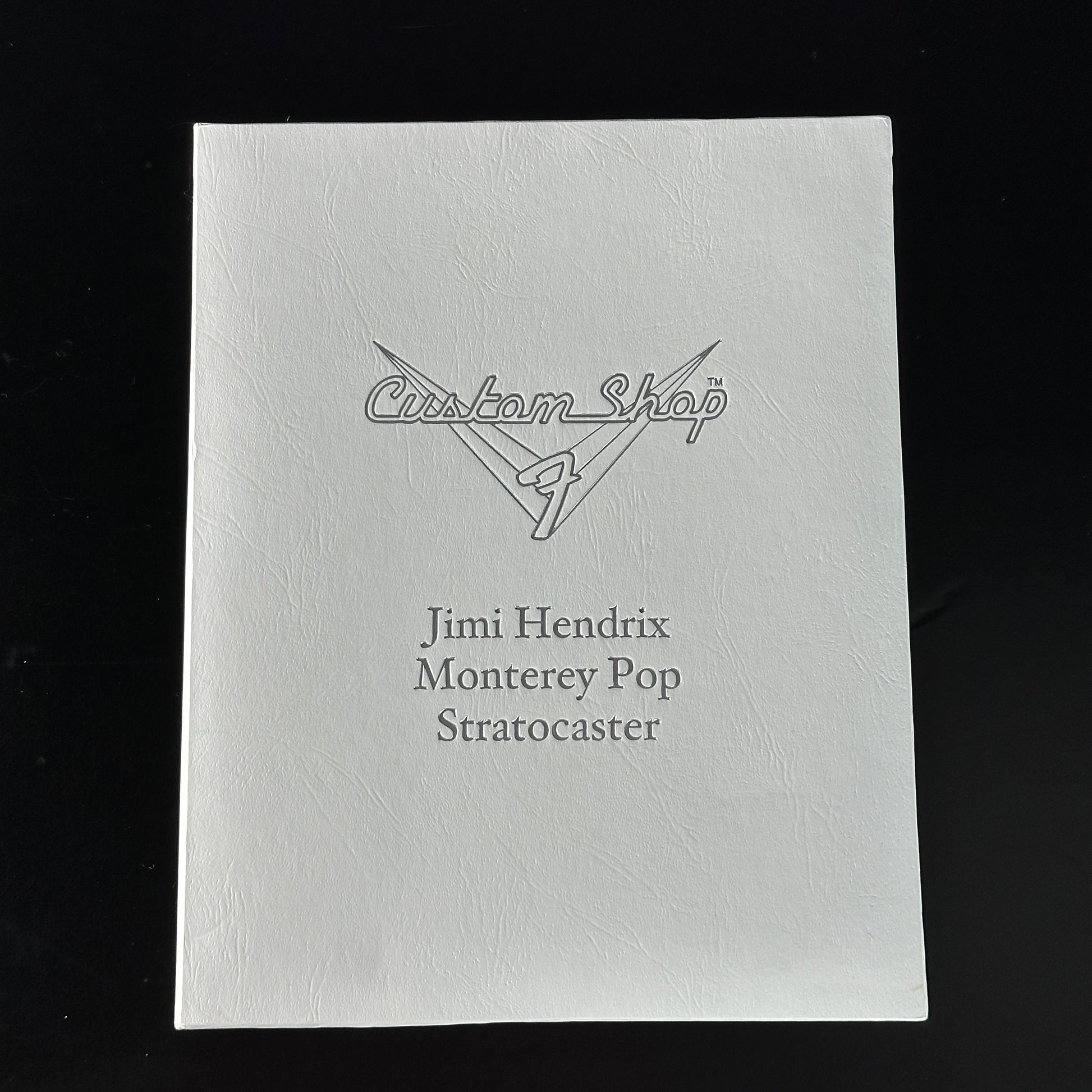 White guitar case with 'Custom Shop' and 'Jimi Hendrix Monterey Pop Stratocaster' text on a black background