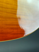 Close-up of a glossy wooden curved surface with a warm amber-brown finish and visible wood grain, against a dark gray background.