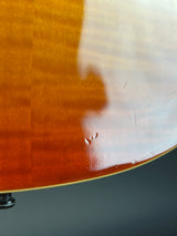Close-up of the glossy back of an acoustic guitar showing the natural wood grain and a small chip in the finish.
