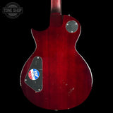 The back of a red electric guitar with a glossy cherry red finish, showing a black pickguard, silver hardware, and a circular Tone Shop watermark in the top left corner.