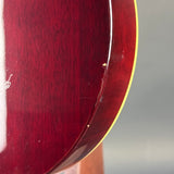 Close-up of the glossy dark red wood body of an electric guitar, showing the grain and a thin yellow binding edge against a gray background.