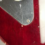 Close-up of a red electric guitar body with a black pickguard showing visible scratches and wear.