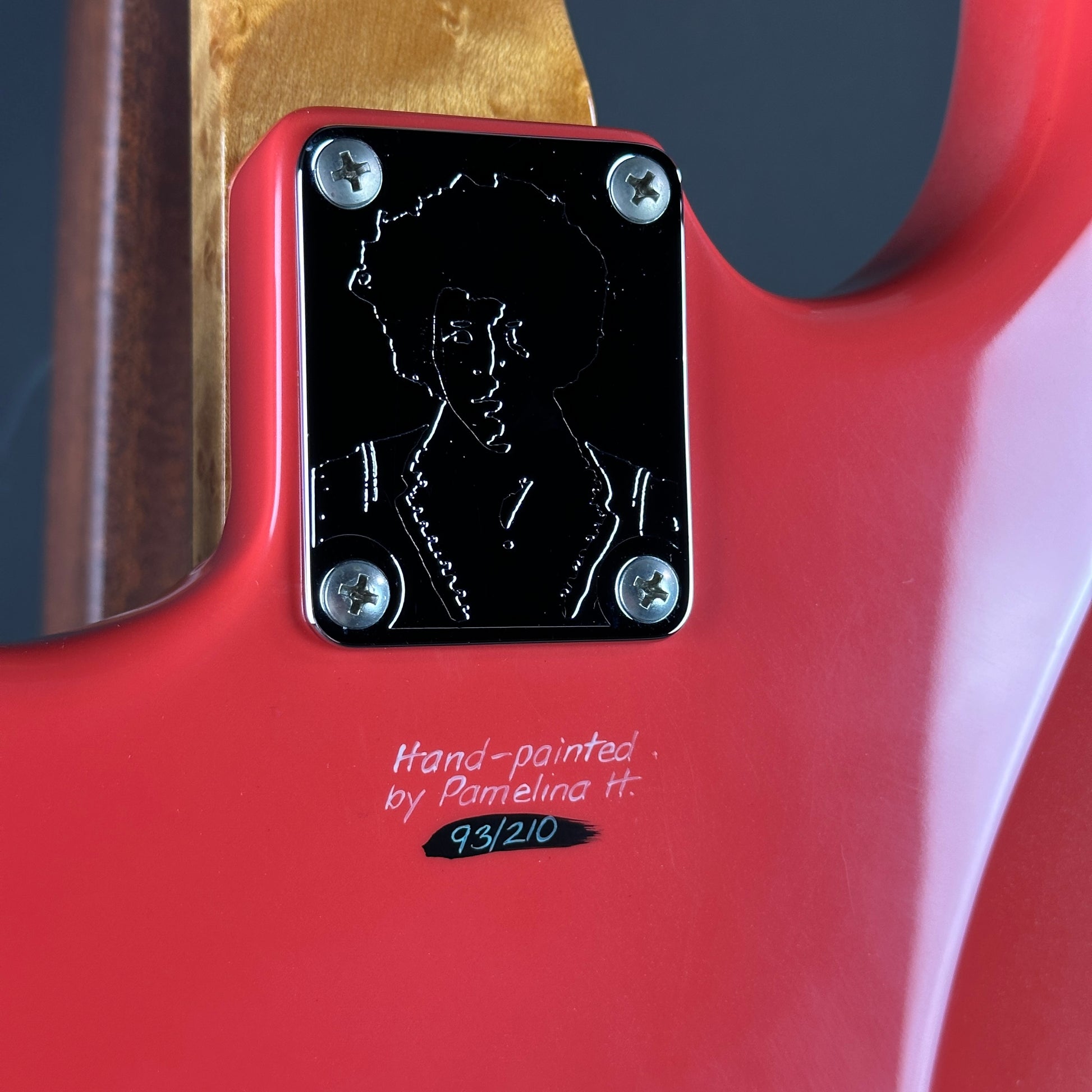 Close-up of a red guitar with a black label and hand-painted signature.