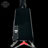 The back view of a black electric guitar resting on a stand against a black background, with a Tone Shop watermark in the top-left corner.