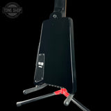 The back view of a black electric guitar resting on a black stand, showing the output jack and red mounting bracket against a solid black background.