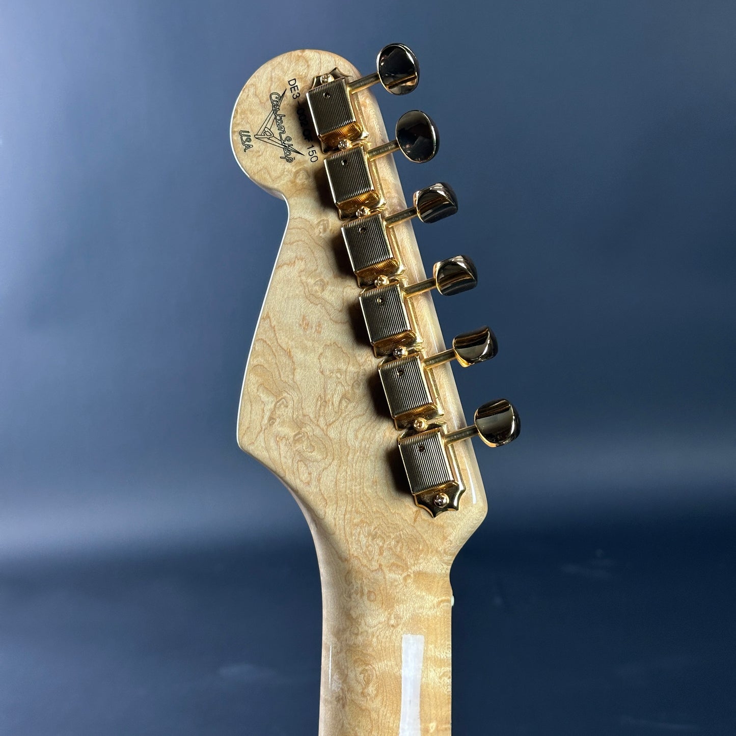 Close-up of a guitar headstock with tuning pegs on a blue background