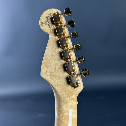 Close-up of a guitar headstock with tuning pegs on a blue background