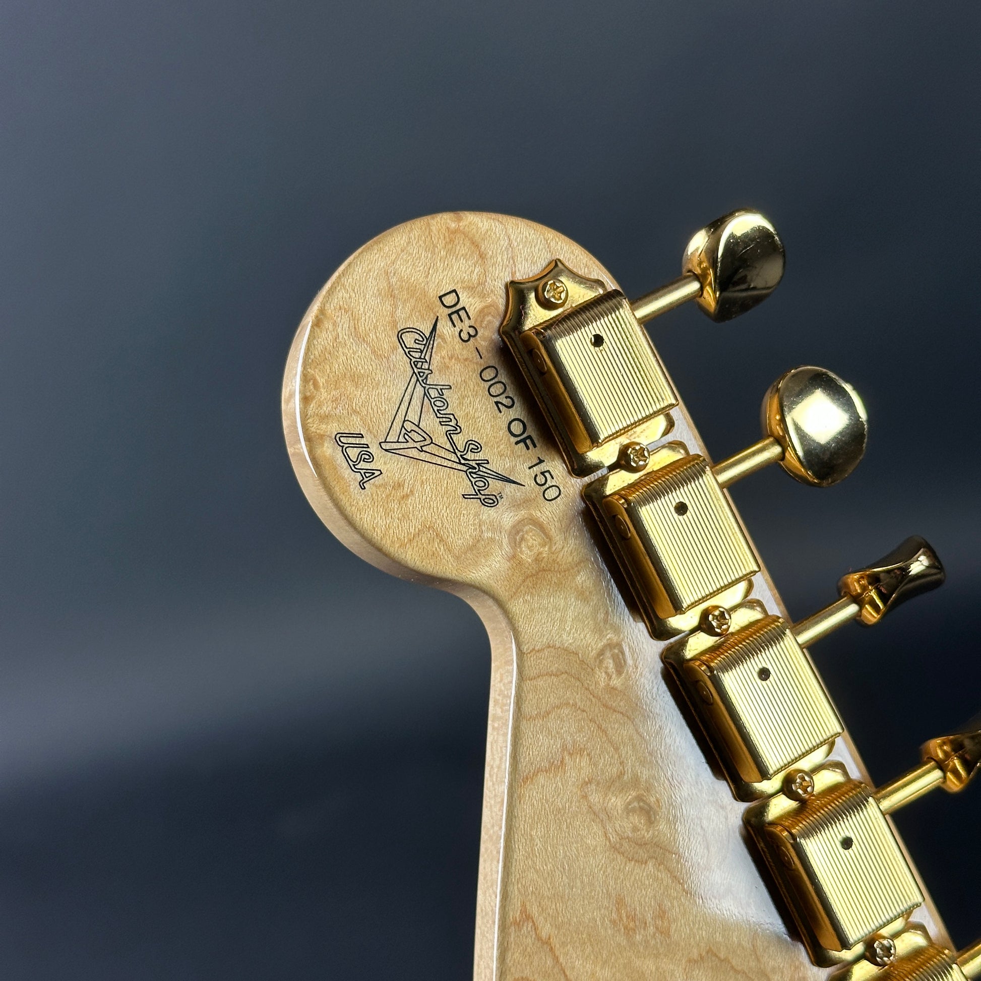 Close-up of a guitar headstock with tuning pegs on a dark background