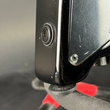 Close-up detail of a black guitar body showing a side screw, edge profile, and part of a red headstock clamp or stand.