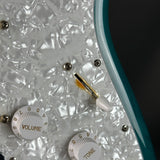 Close-up of a guitar with volume and tone knobs on a textured white surface.