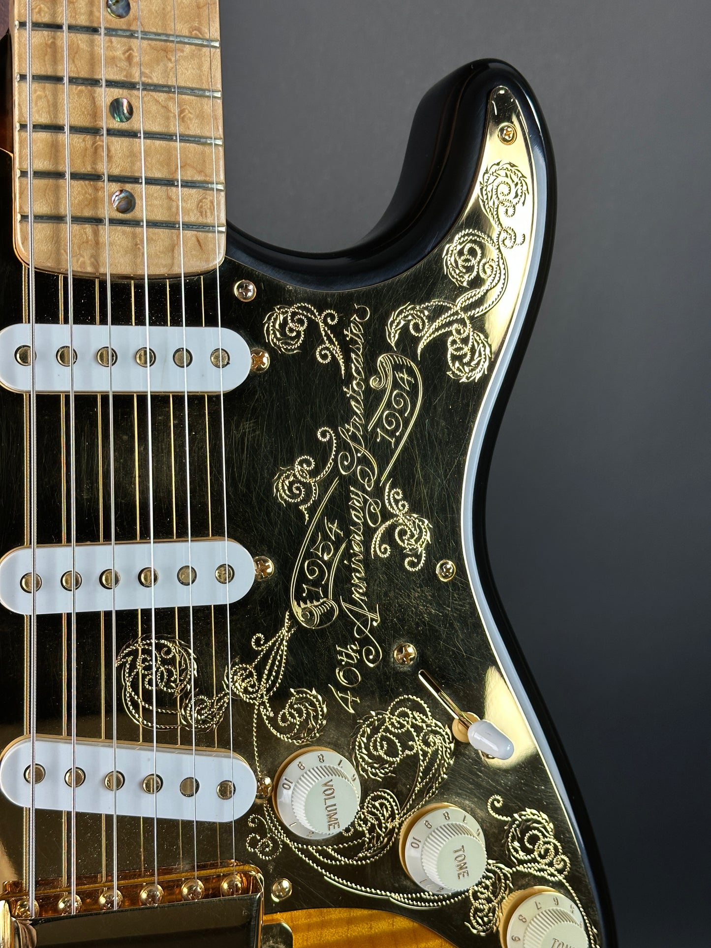 Close-up of a black electric guitar with gold detailing on a dark background