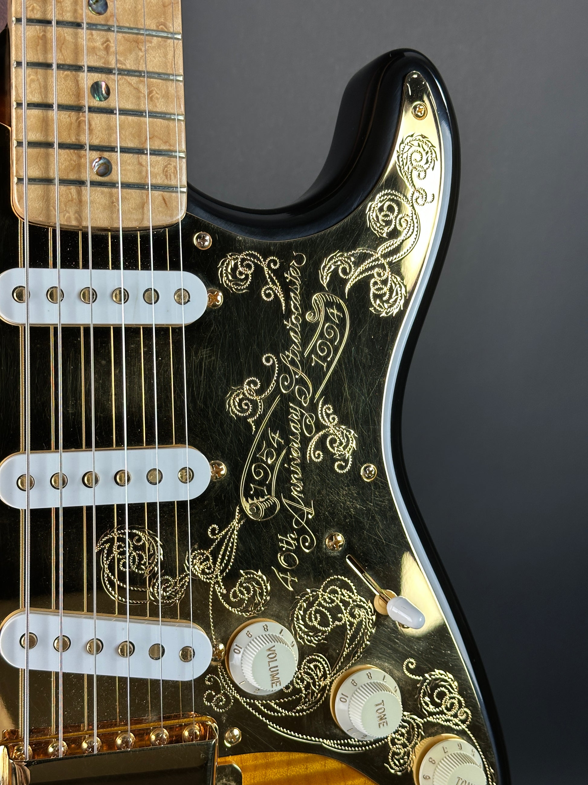 Close-up of a black electric guitar with gold detailing on a dark background
