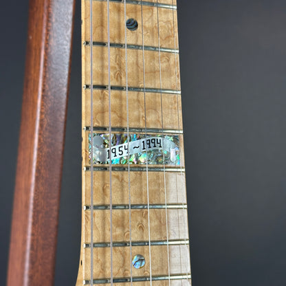 Close-up of a guitar neck with a label indicating the years 1954 to 1994 on a dark background.