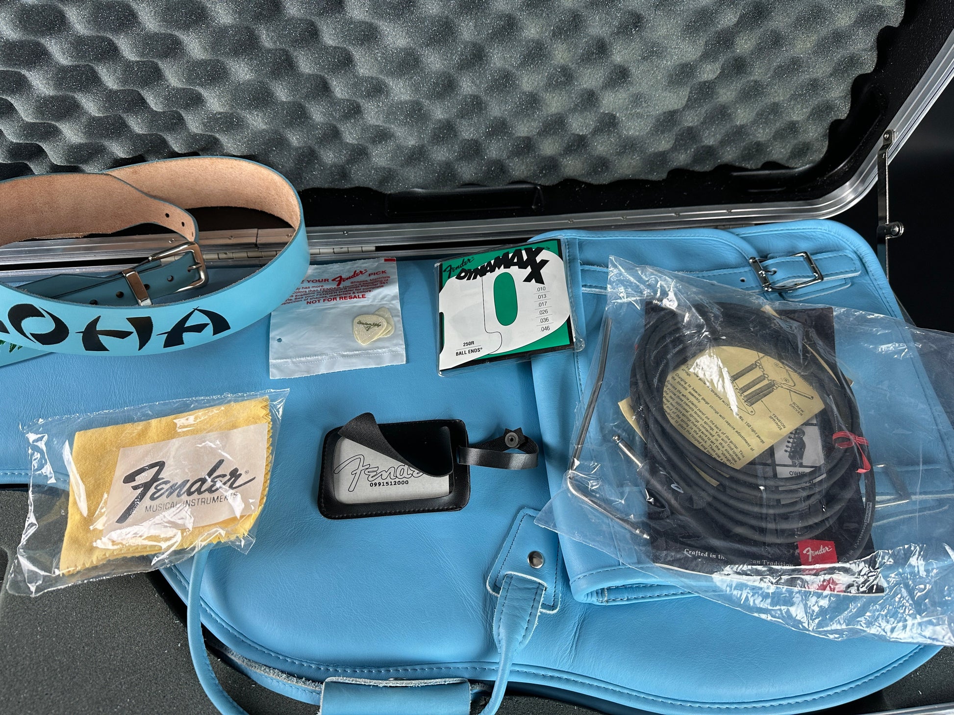 Blue guitar case with Fender accessories including a cable, strap, and cleaning cloth.