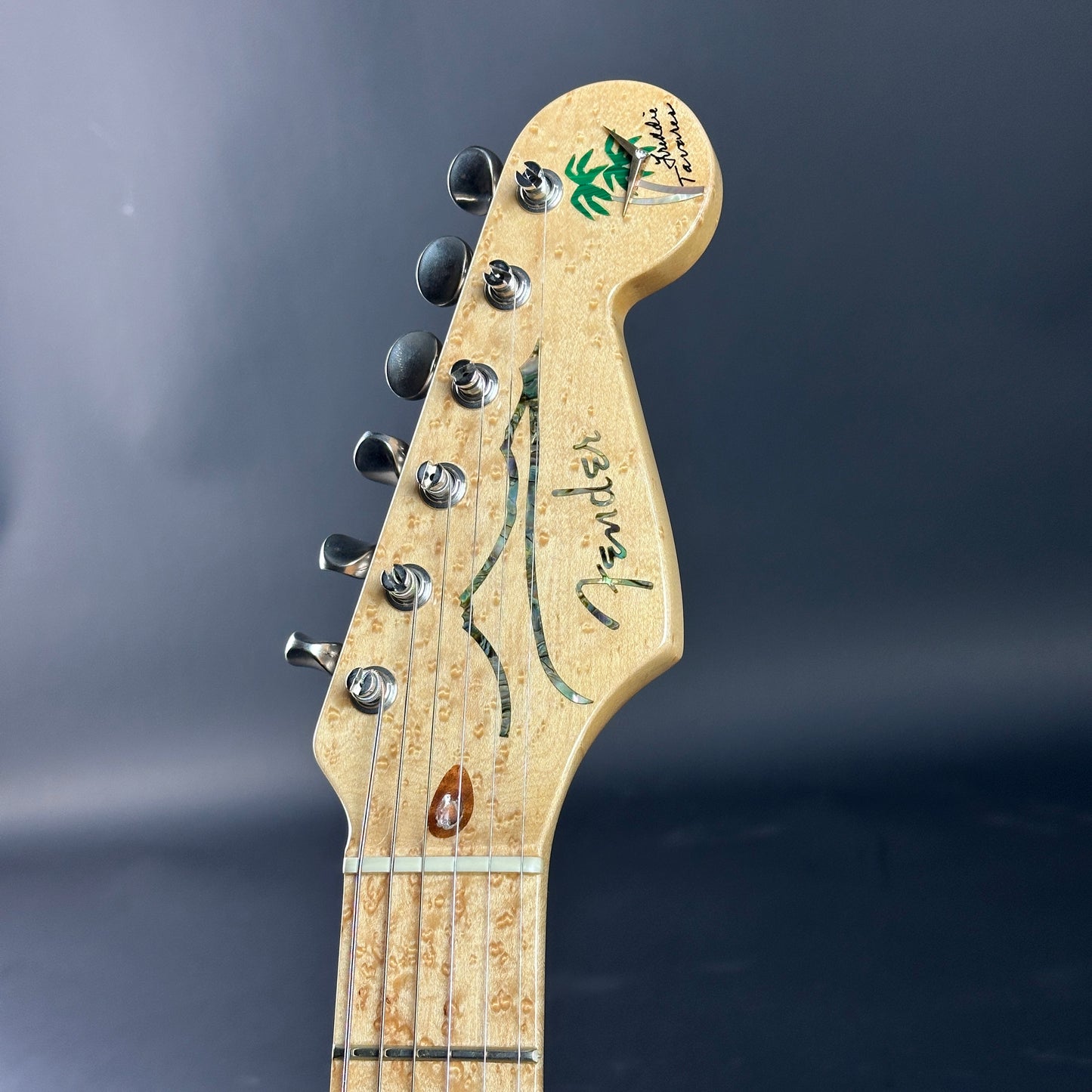 Close-up of a guitar headstock with brand logo and signature on a dark background