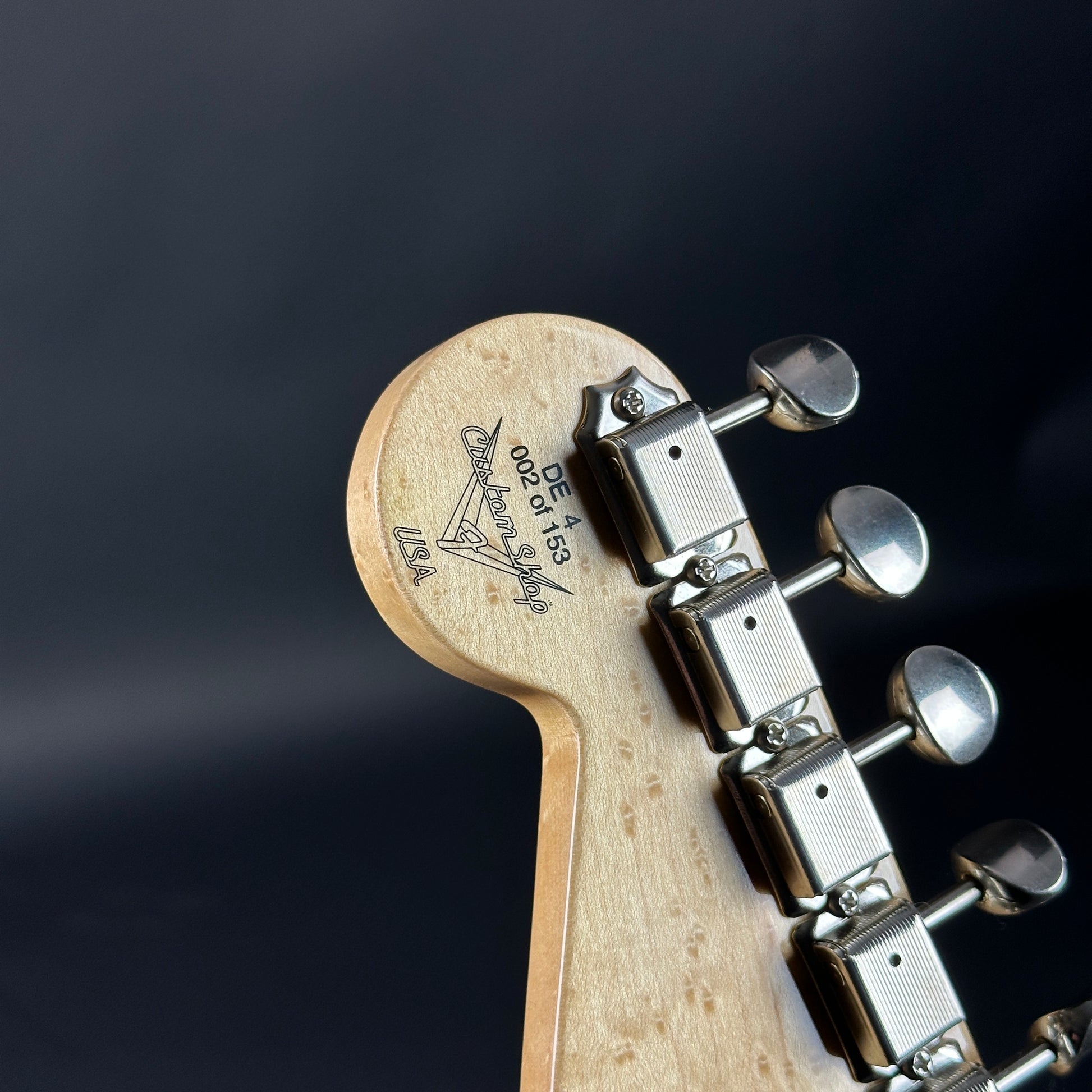 Close-up of a guitar headstock with tuning pegs on a dark background