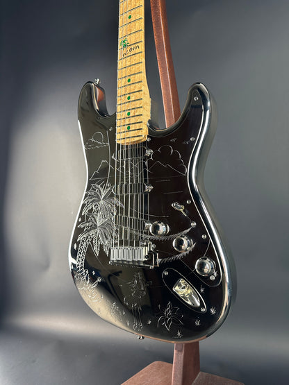 Close-up of a black electric guitar with intricate designs on a gray background