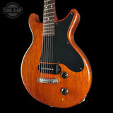 Electric guitar with a wooden finish on a black background, featuring the Tone Shop logo.