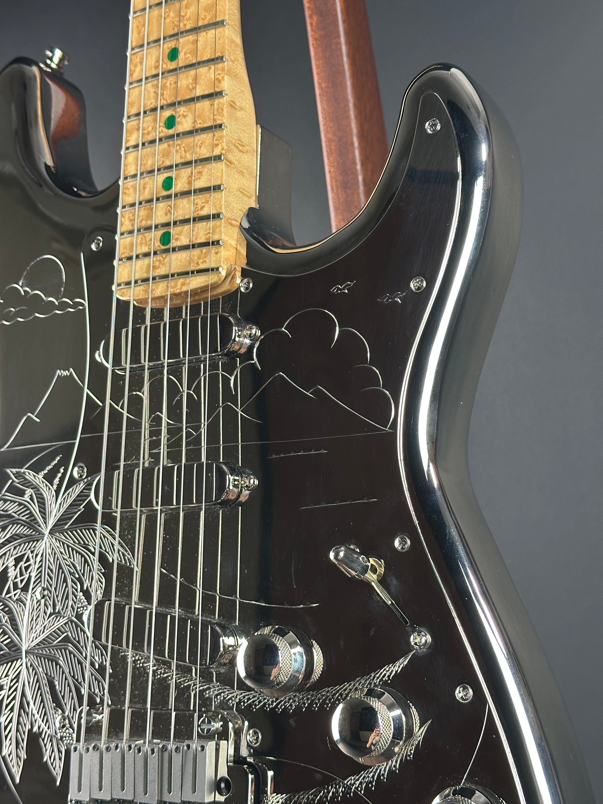 Close-up of a black electric guitar with detailed engravings on a gray background
