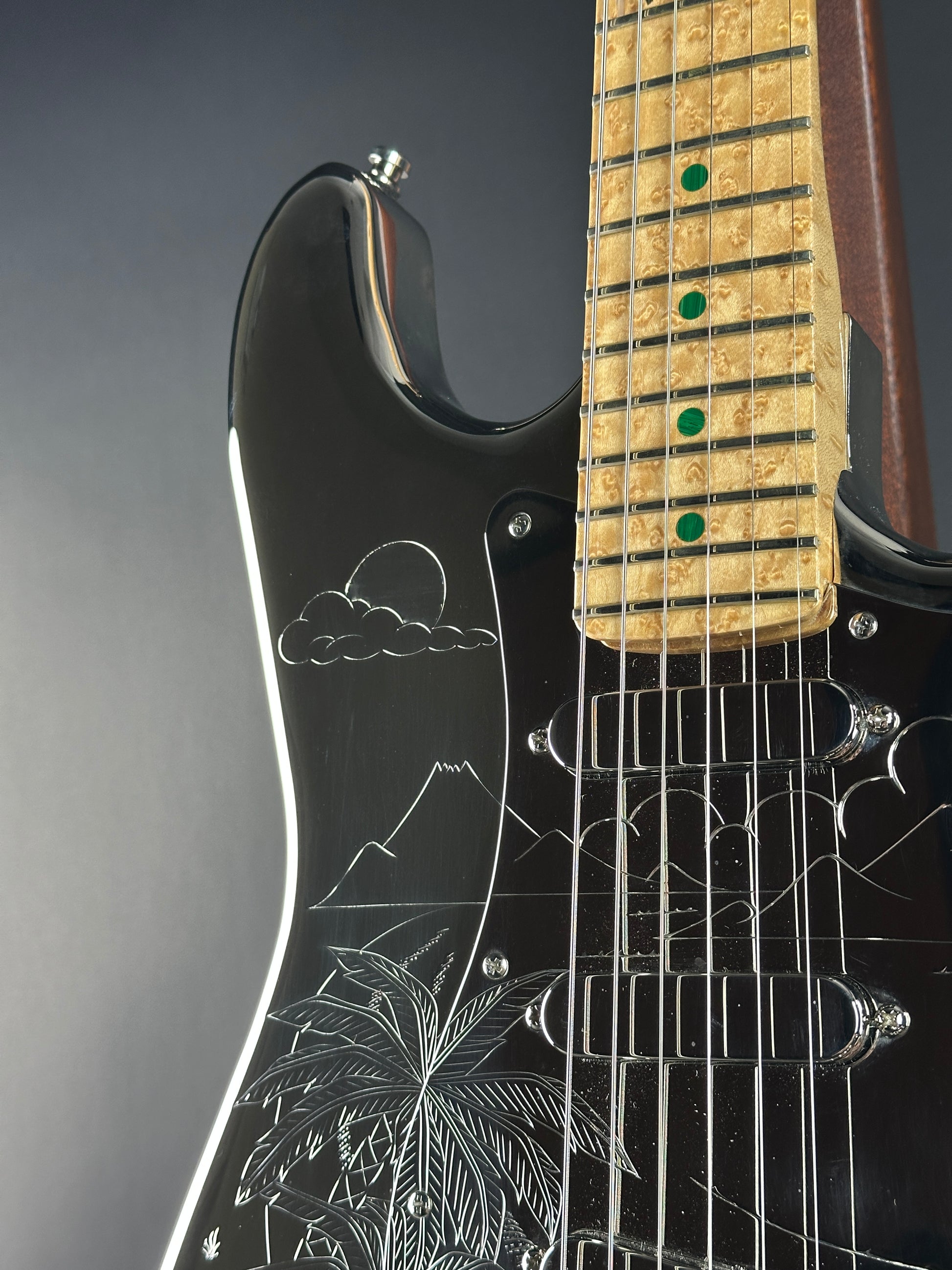 Close-up of a black electric guitar with engraved designs on the body.