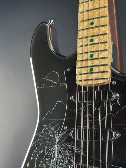 Close-up of a black electric guitar with engraved designs on the body.