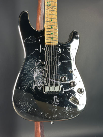 Close-up of a black electric guitar with engraved designs on a dark background