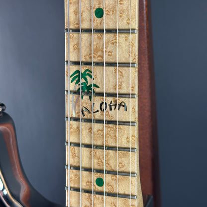 Close-up of a guitar neck with 'Aloha' and palm tree design on a dark background