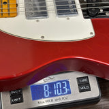 A close-up of a red electric guitar body resting on a digital scale displaying 8.103 oz, with the white pickguard and part of the neck visible.