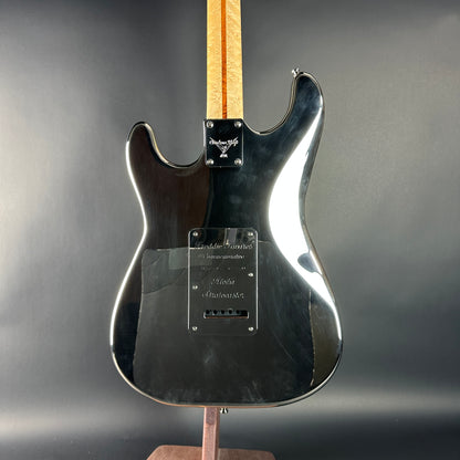 Black electric guitar on a stand with a gray background