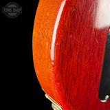 Close-up of a red guitar with visible wood grain texture on a black background.