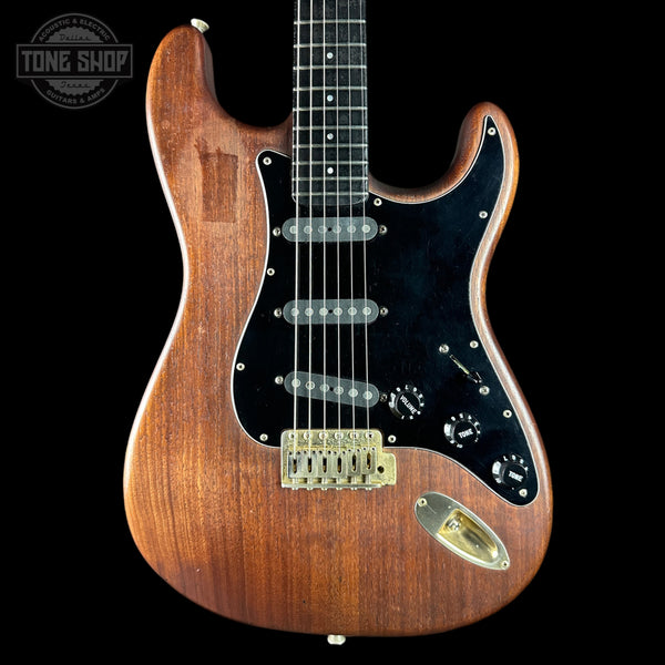 Wooden electric guitar with a black pickguard on a black background, featuring the Tone Shop logo.