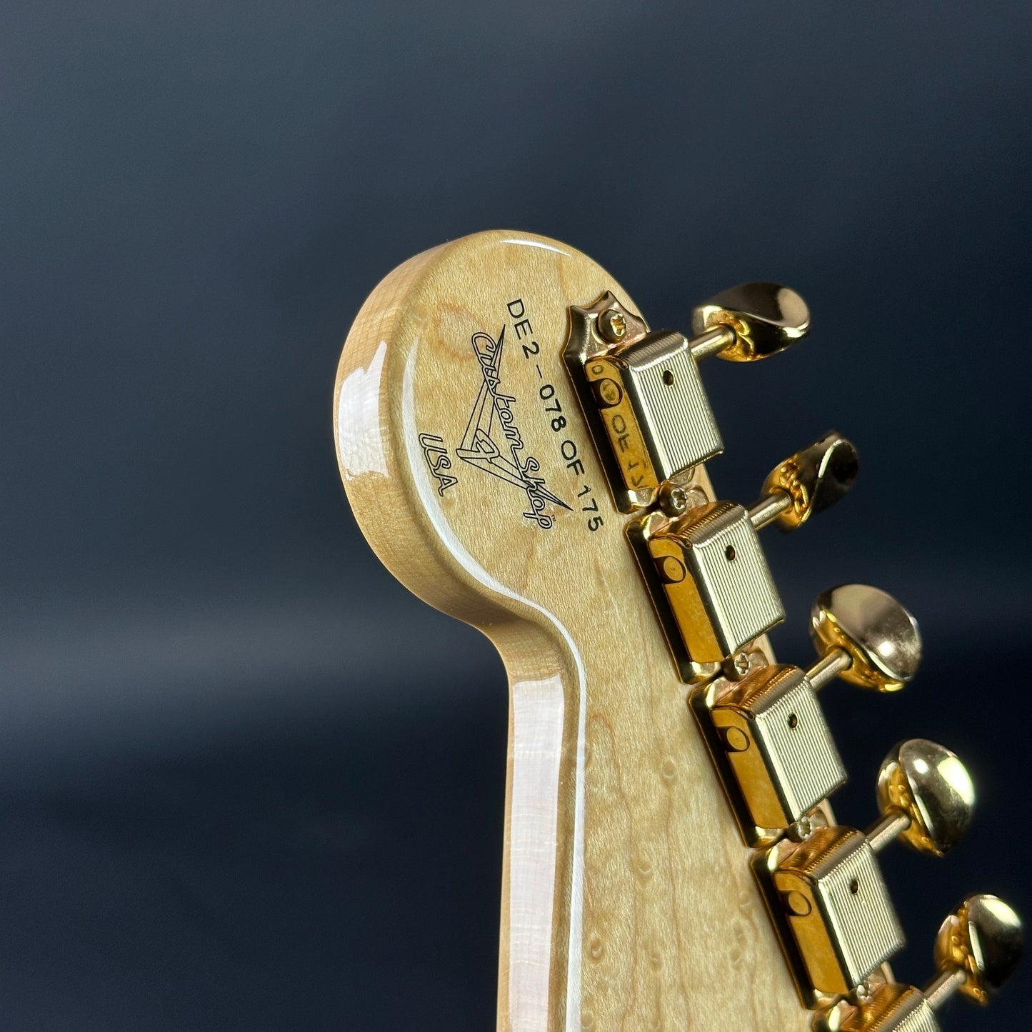 Close-up of a guitar headstock with gold tuning pegs on a dark background