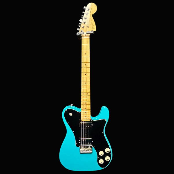 Blue electric guitar with a black pickguard on a gray background