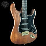 Wooden electric guitar with a black pickguard on a black background, featuring the Tone Shop logo.