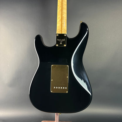 Black electric guitar with a blonde fretboard on a gray background