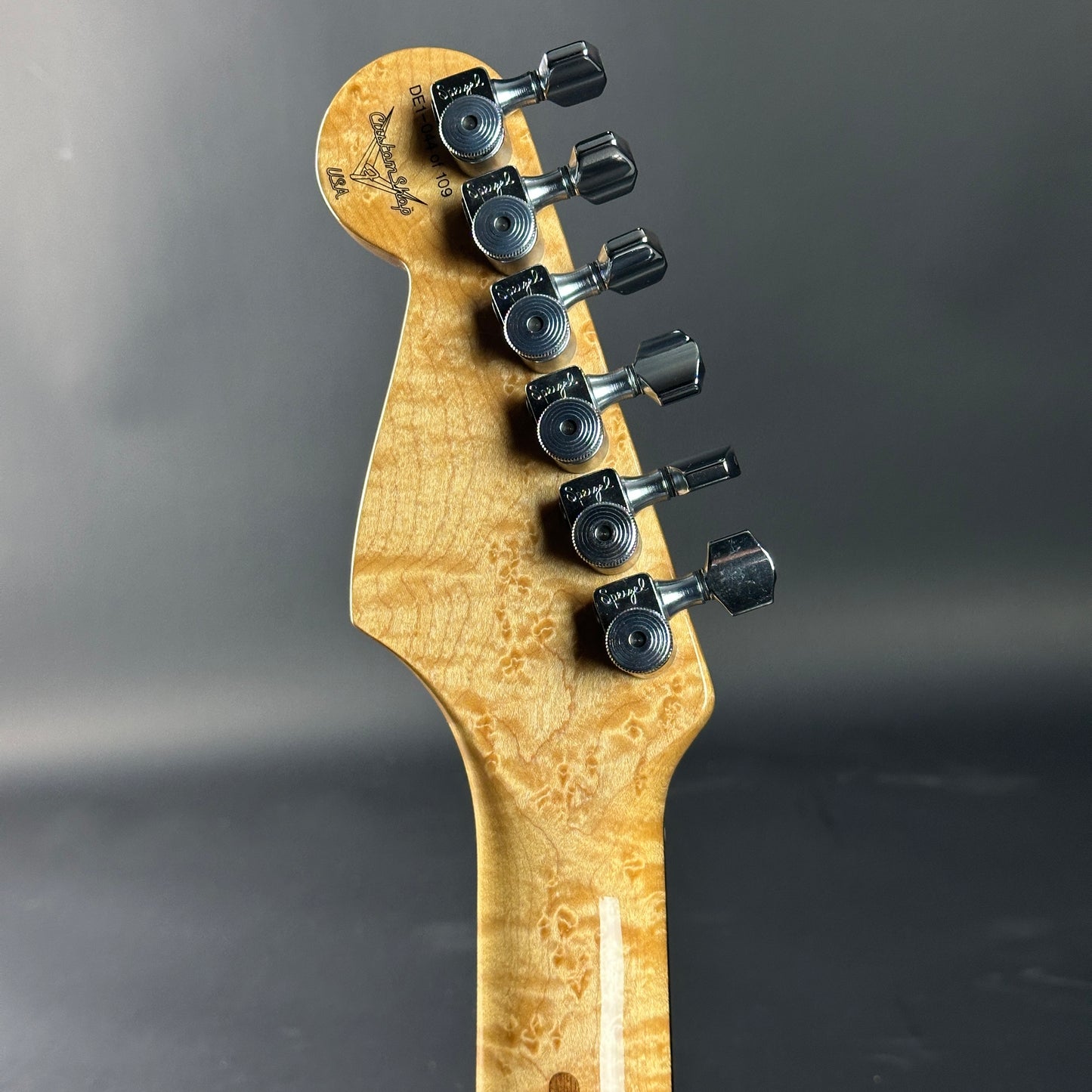 Guitar headstock with tuning pegs on a gray background