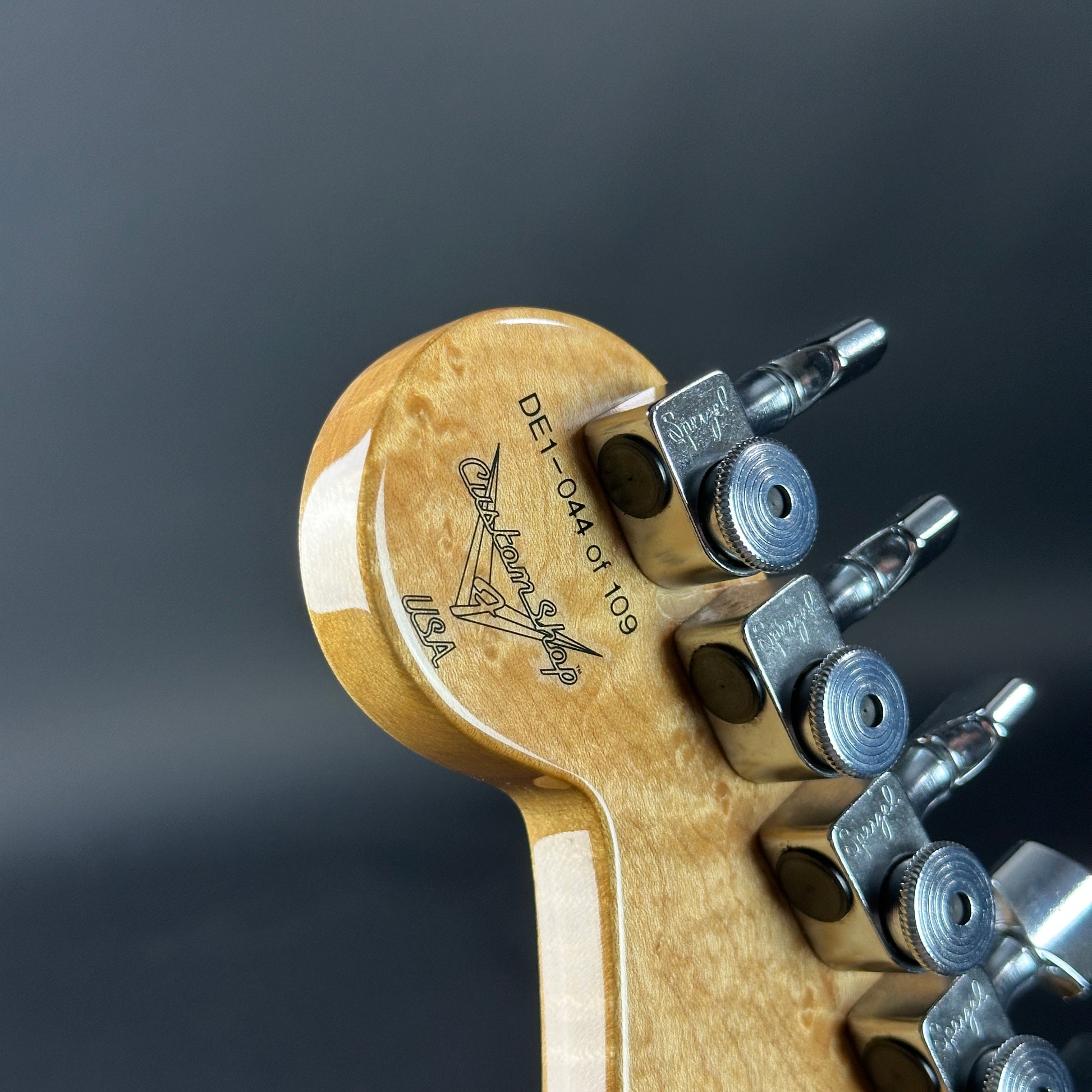 Close-up of a guitar headstock with tuning pegs on a dark background