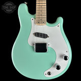 Turquoise electric guitar with a white pickguard on a black background, featuring 'Tone Shop' branding.
