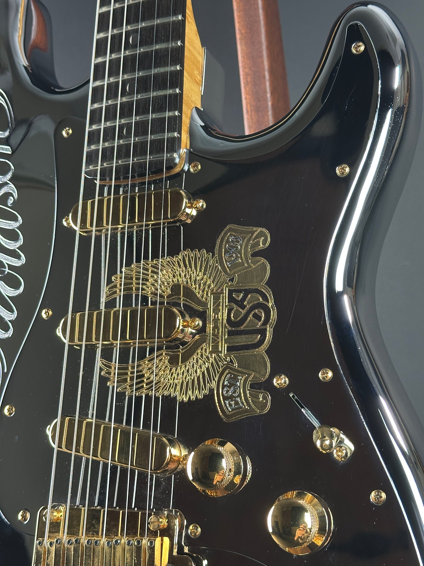 Close-up of a black electric guitar with gold hardware and logo.