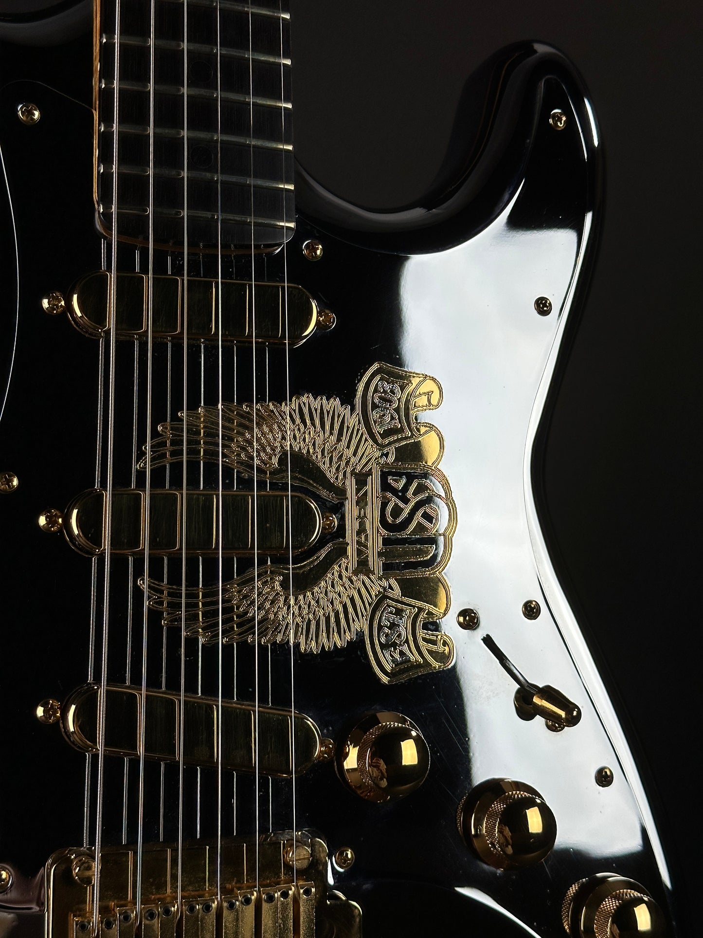 Close-up of a black electric guitar with a gold logo on a dark background