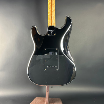 Black electric guitar on a stand against a gray background
