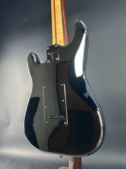 Close-up of a black electric guitar with a wooden fretboard on a dark background