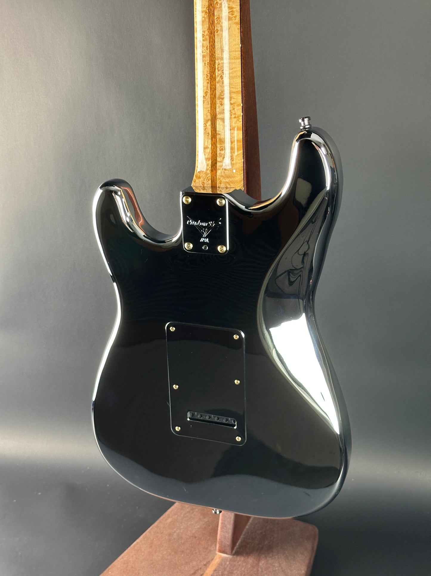 Close-up of a black electric guitar with a wooden neck on a gray background